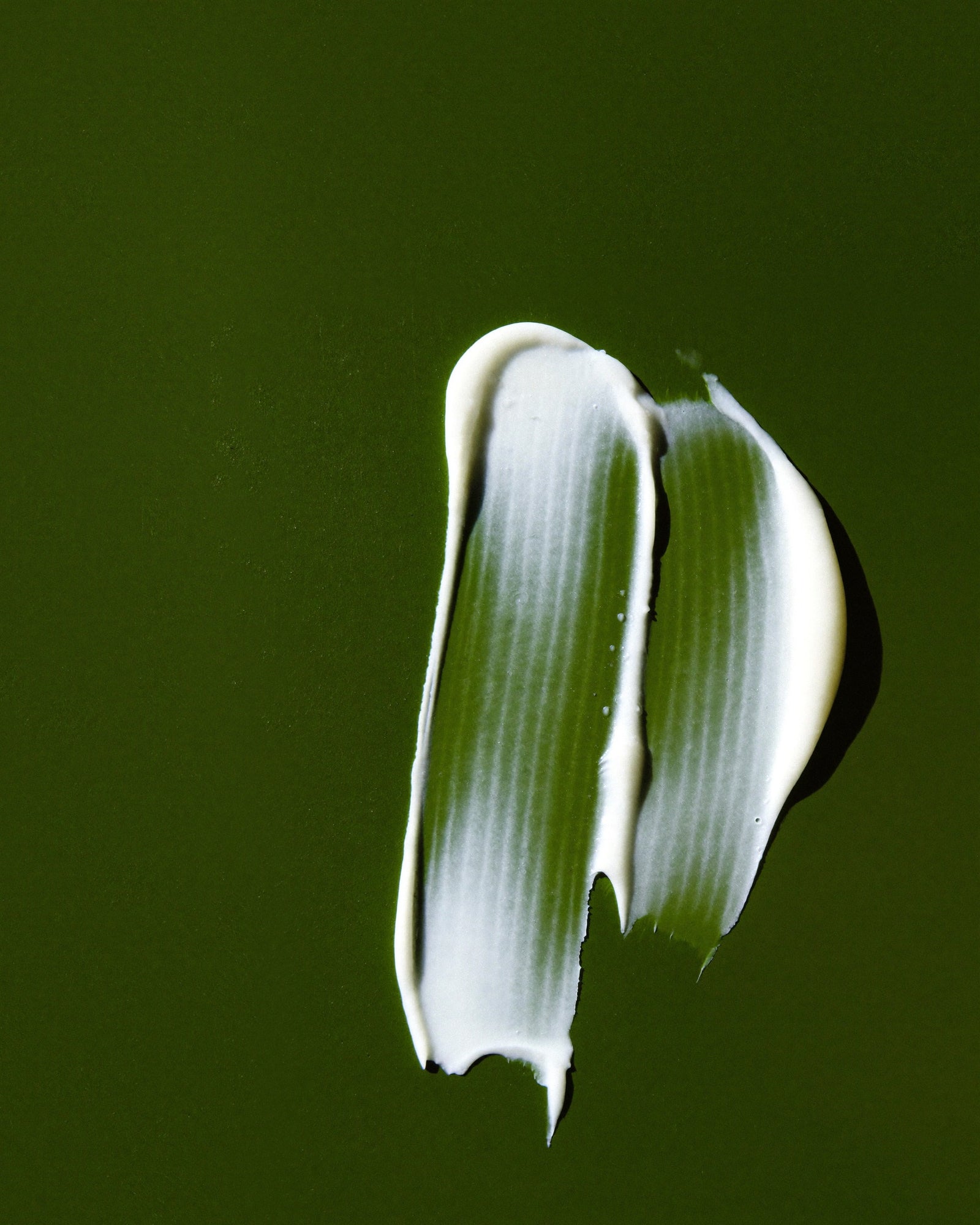 Two swipes of white Body Balm on an olive surface