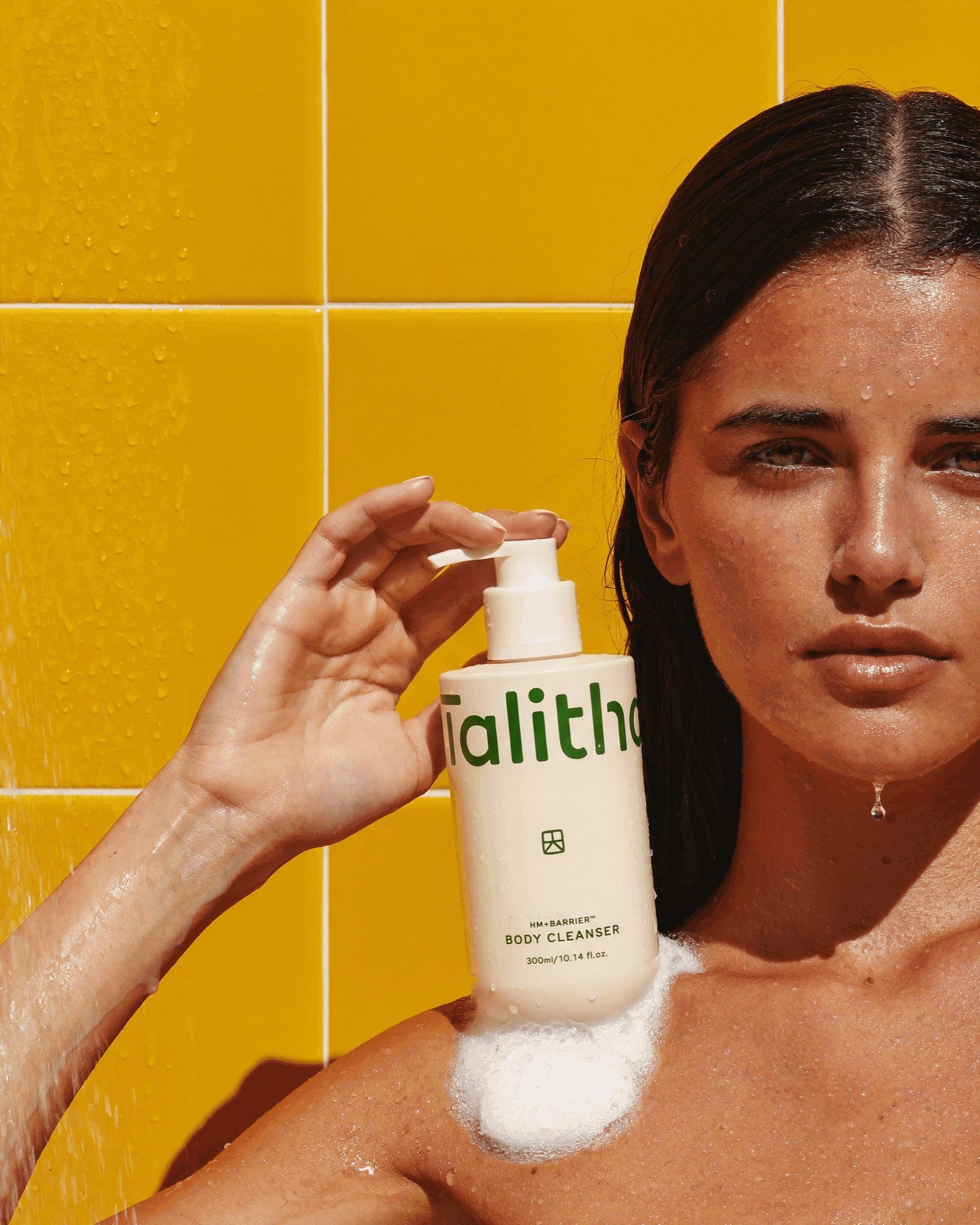 A model in the shower holding Body Cleanser, lather on her shoulder