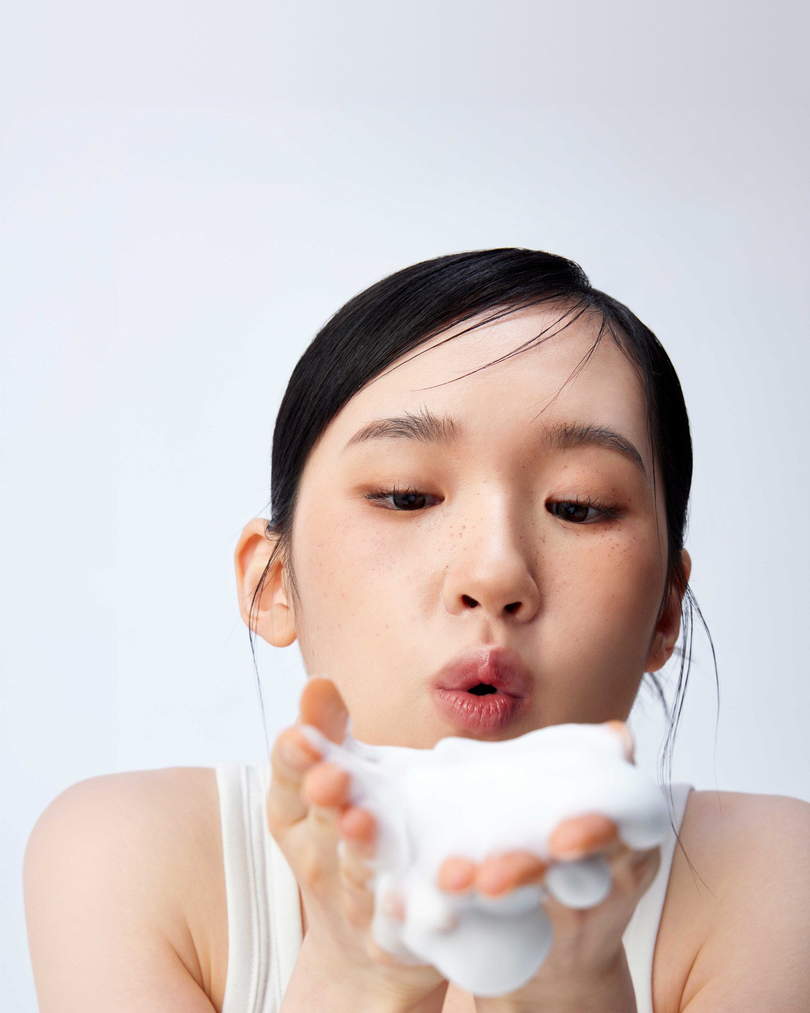 A model blowing a handful of Face Cleanser foam