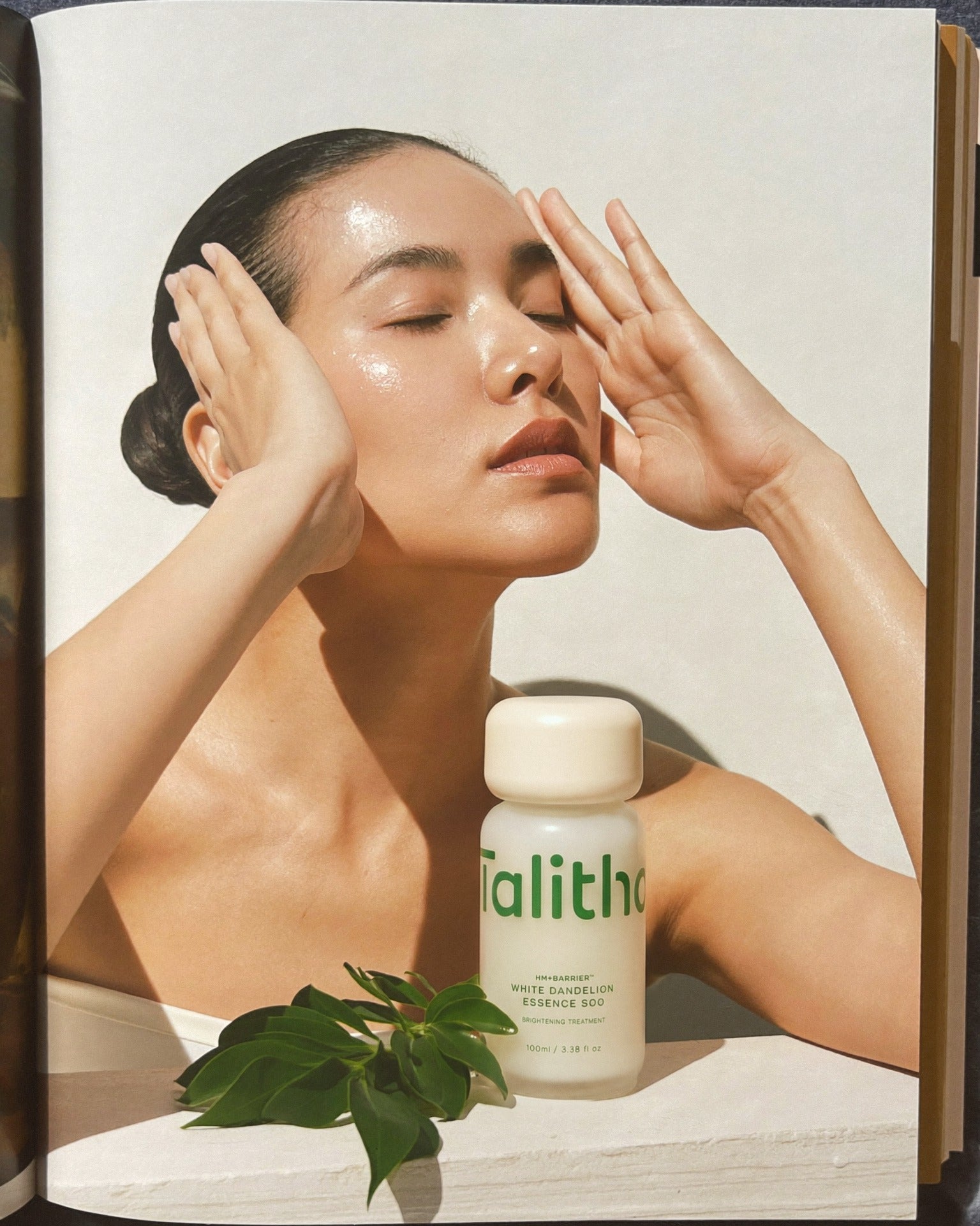 Essence Soo beside a model pressing her temples, printed on a magazine page