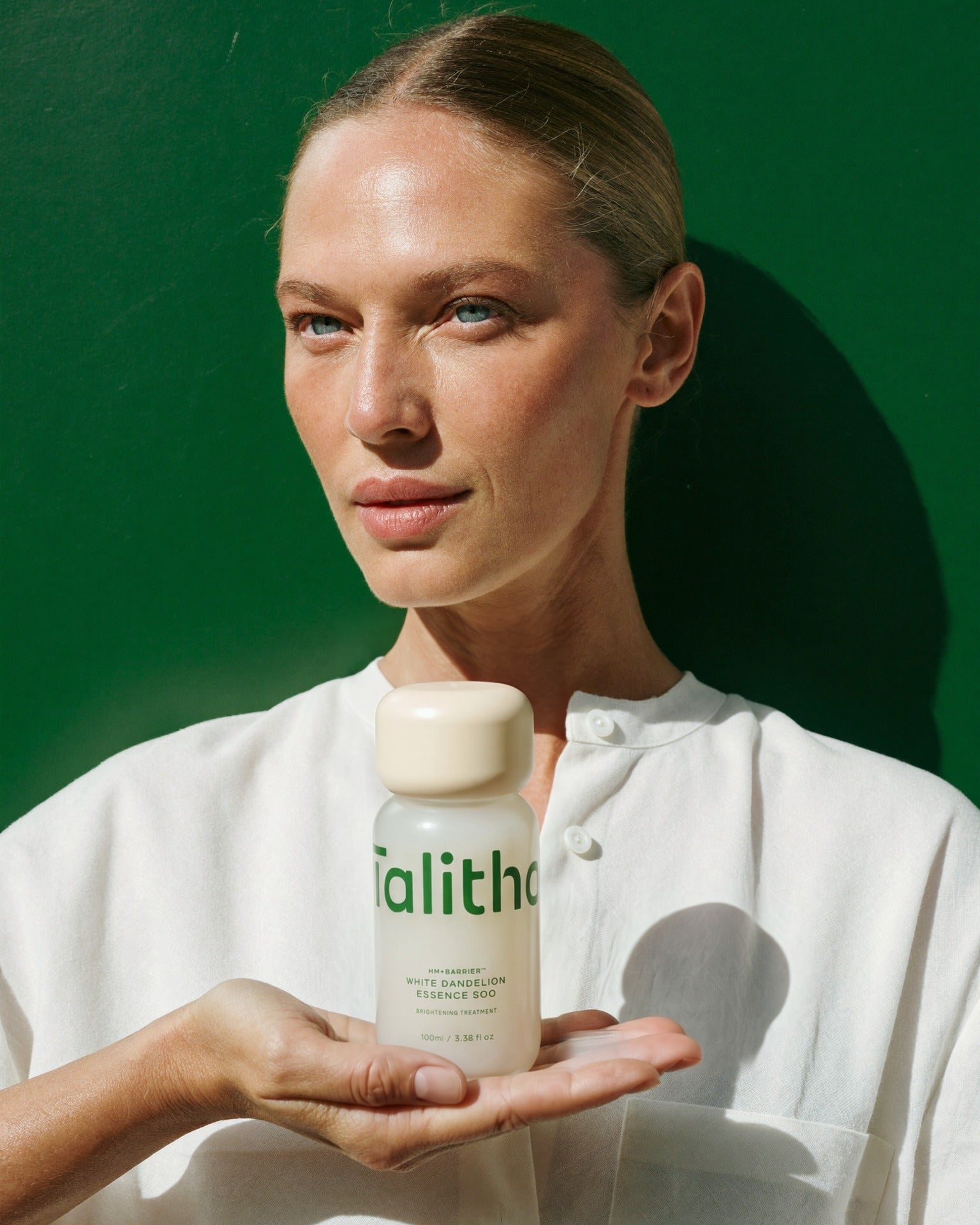 A model holding Essence Soo 100ml in her palm against a green wall